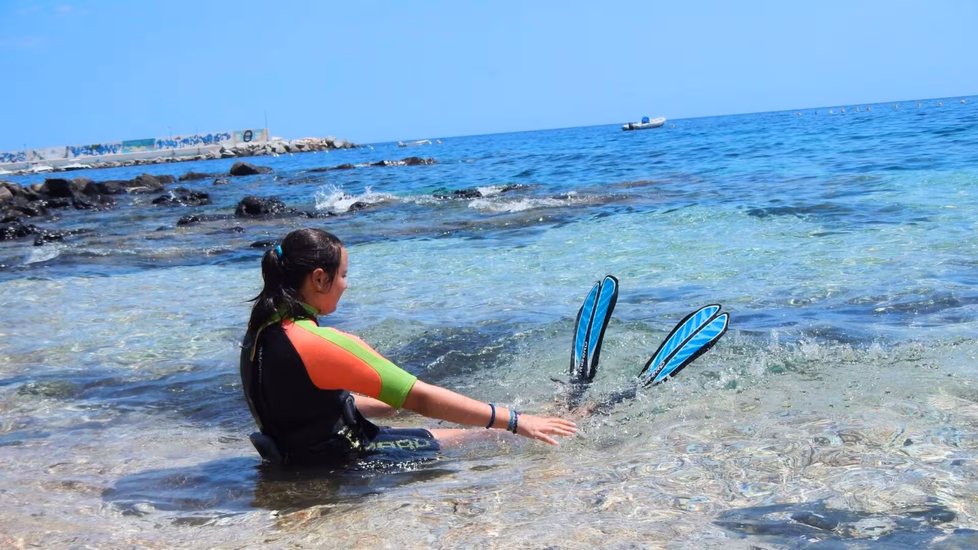 Diver in a colorful wetsuit sits at Cala Gonone's shore, ready for an underwater adventure baptism.