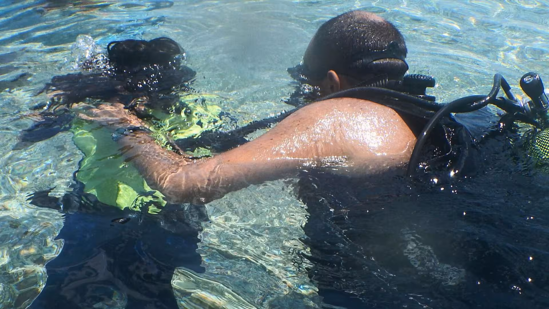 Instructor guides a diver in Cala Gonone during an underwater baptism experience in clear waters.