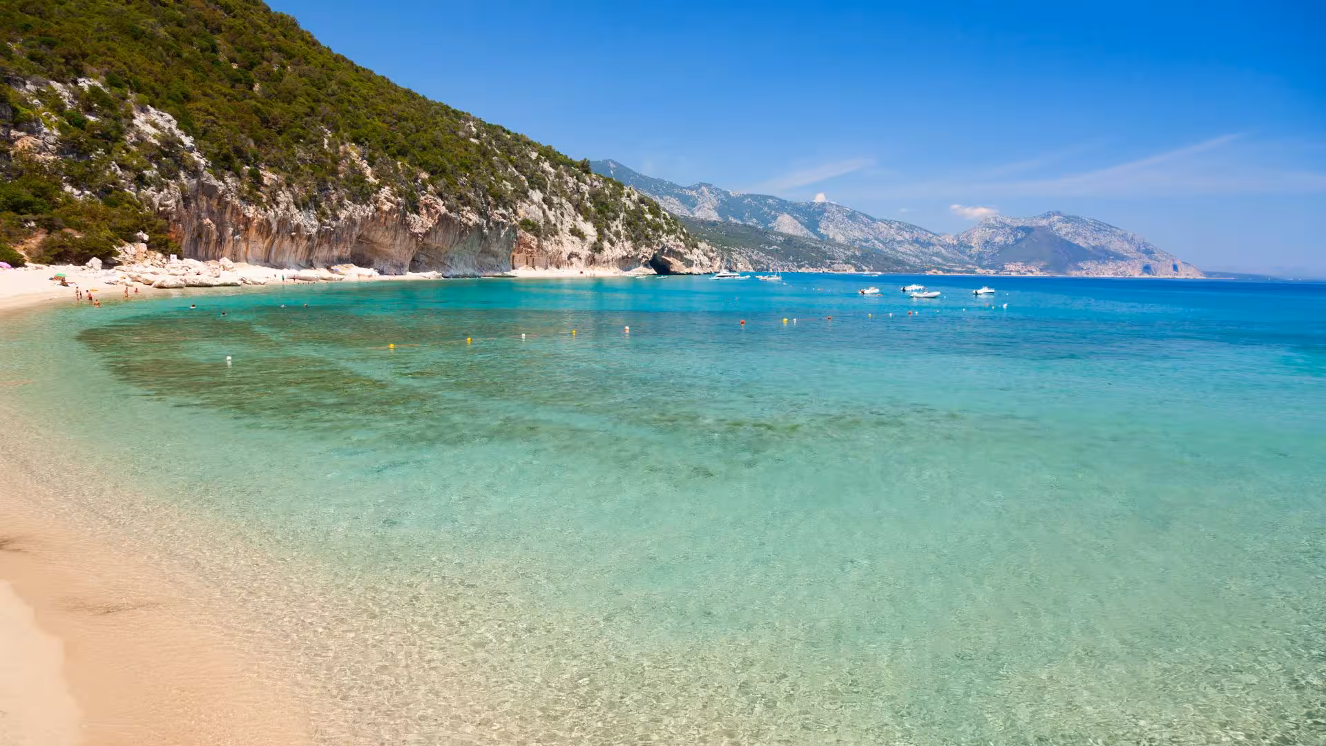 Pristine Cala Luna beach with clear blue waters and distant mountains, accessible via motorboat from Cala Gonone.