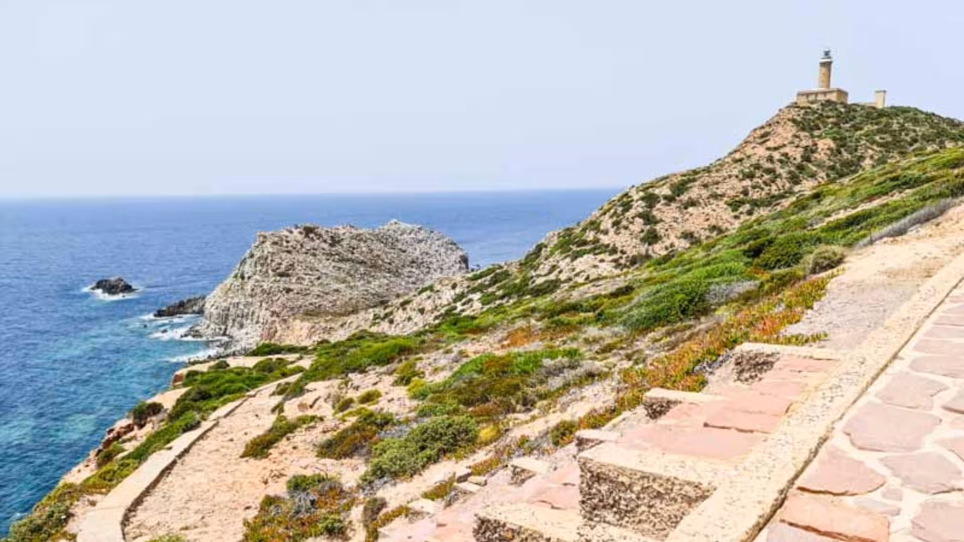 Scenic view of Calasetta's rugged coastline with a lighthouse, ideal for exploration via scooter hire.