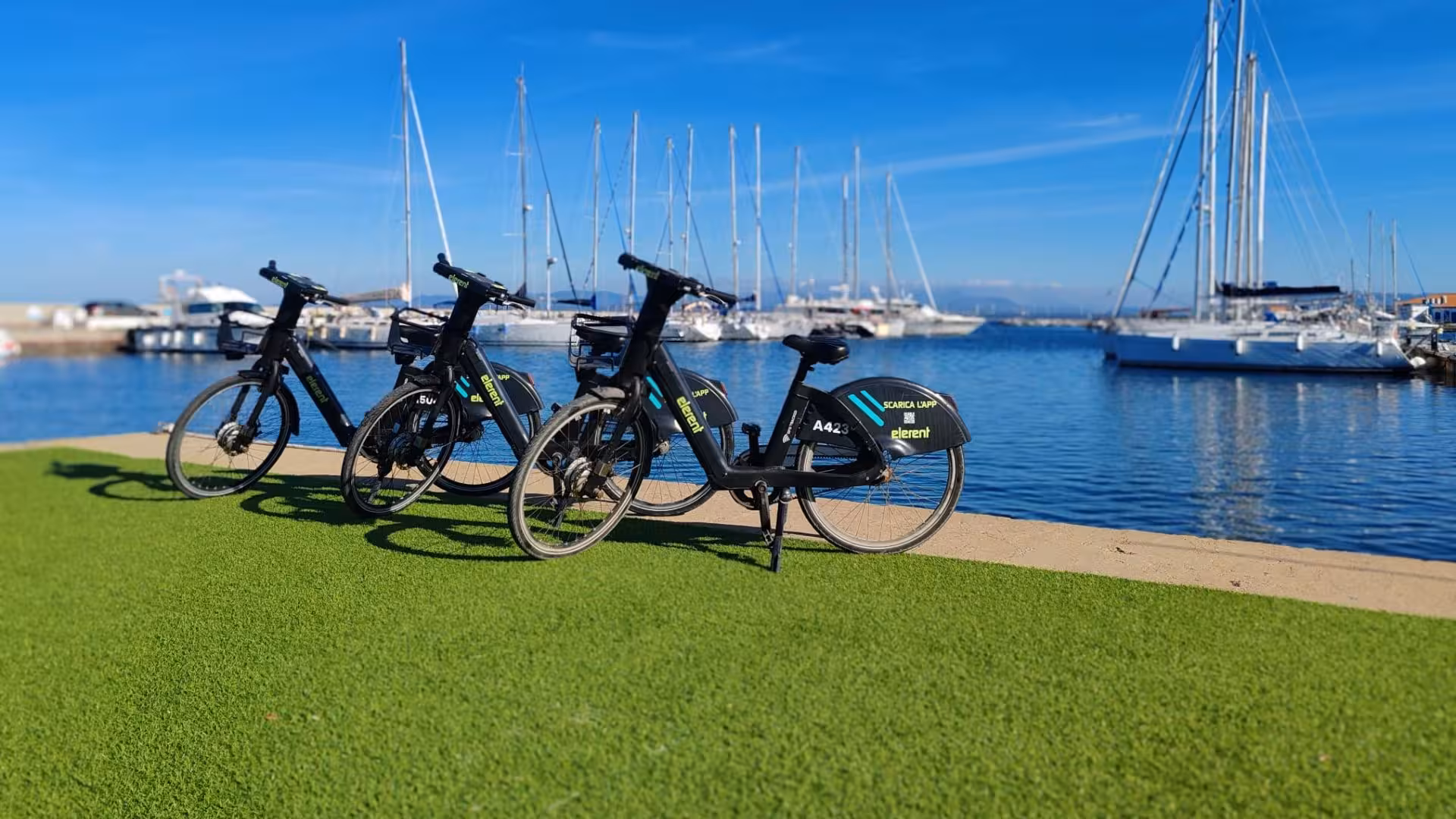 Three e-bikes parked on a grassy area by the Calasetta marina, offering scenic views and sustainable travel options.