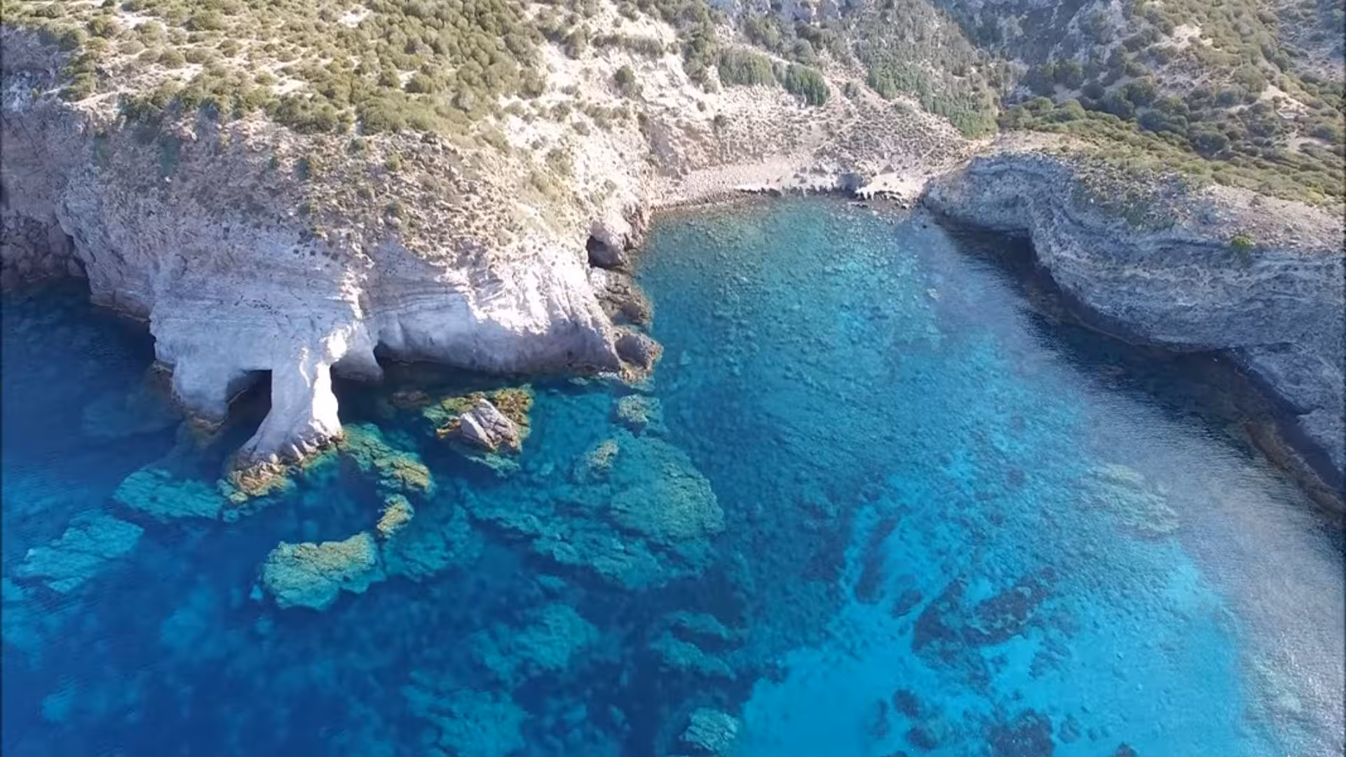 Aerial view of rocky coastline and crystal-clear blue waters in Calasetta, ideal for scenic car hire tours.