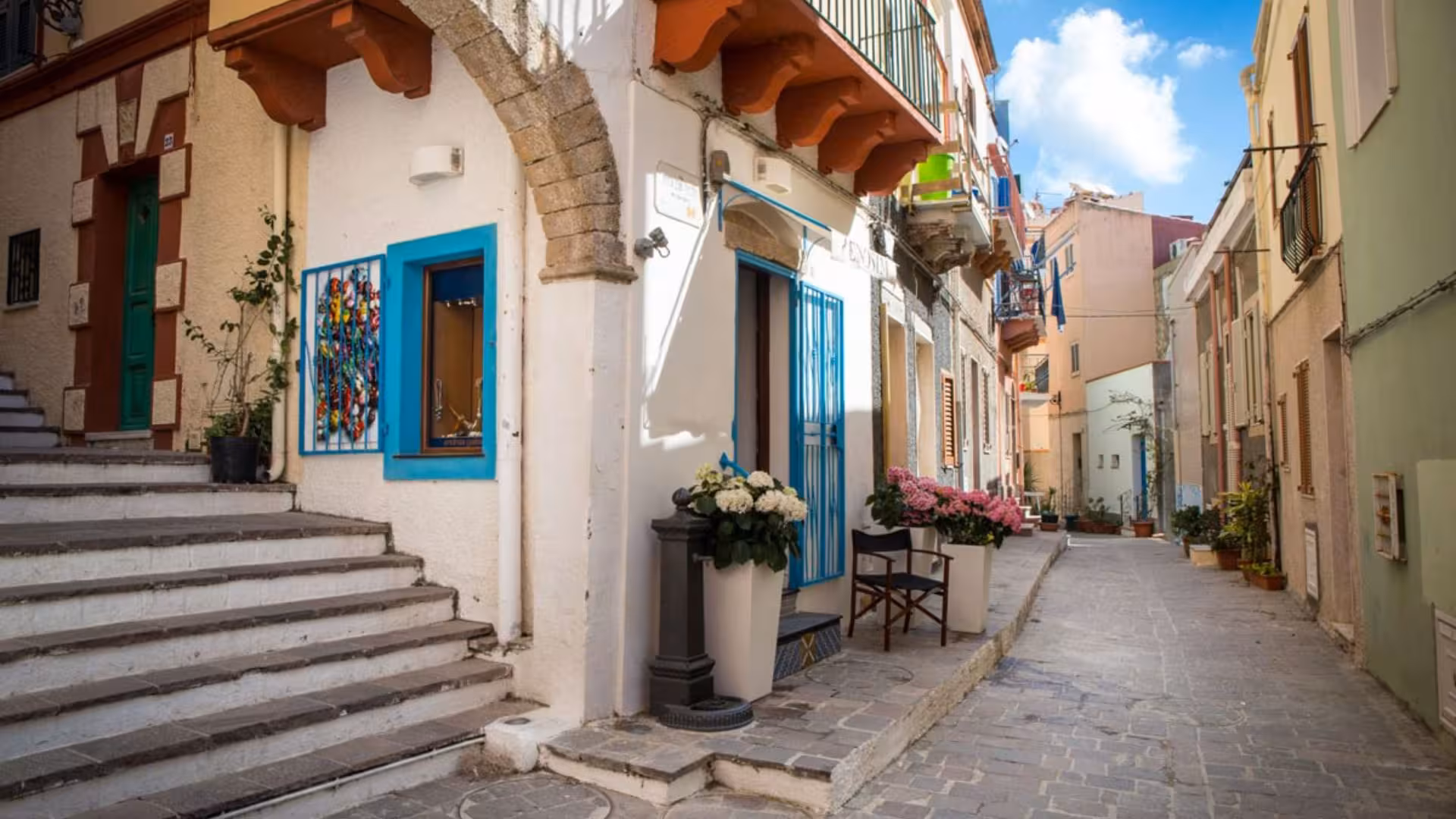 Charming Calasetta street with colorful buildings and flowers, perfect for exploring on a rented scooter.