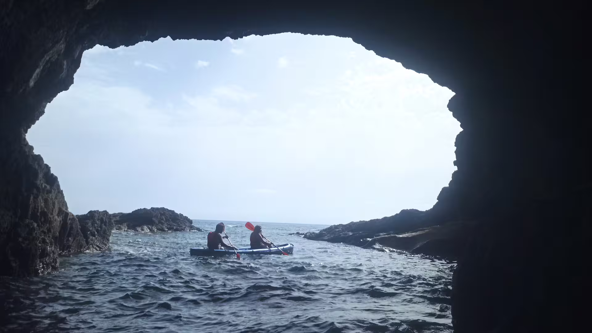 Kayakers paddle through scenic rock formations on the Calheta kayak tour, exploring Madeira's stunning coastal caves and waters.