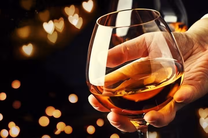 Hand holding a snifter glass of golden Calvados brandy with warm bokeh heart lights in background