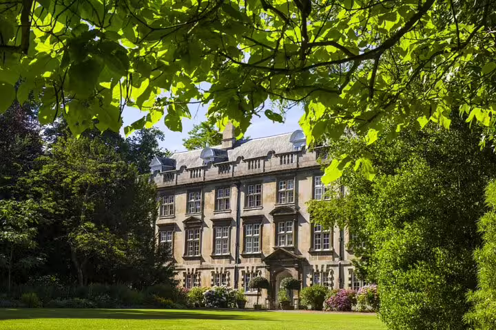 Historic Cambridge college stone mansion surrounded by lush green gardens and trees on a sunny day