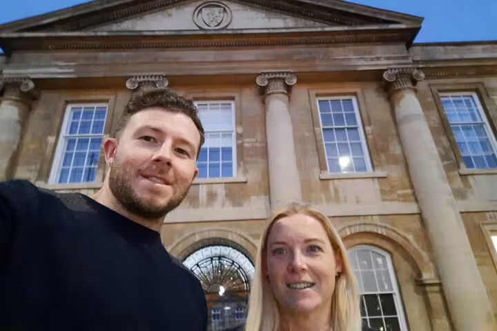 Couple taking selfie in front of historic Cambridge building during self-guided mystery tour