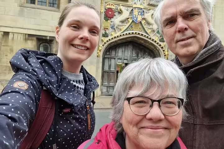 Three tourists smiling in front of an ornate Cambridge college gate during a self-guided walking tour