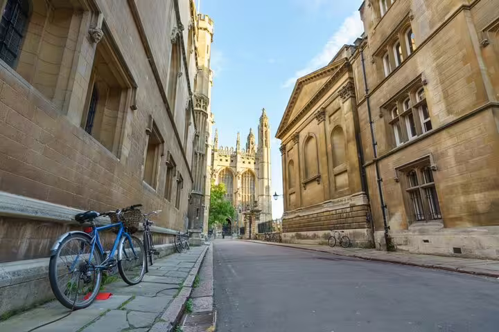 Historic Cambridge university buildings and Gothic chapel along a quiet cobblestone street with parked bicycles