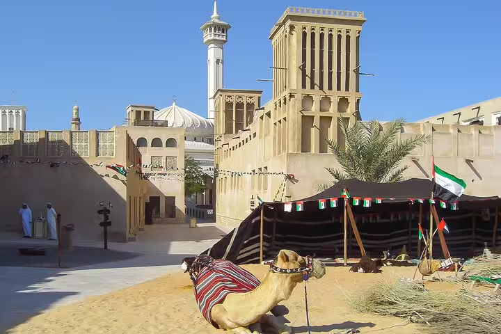 Traditional camel resting in the historic Al Fahidi District, Dubai, with wind towers and a mosque in the background.