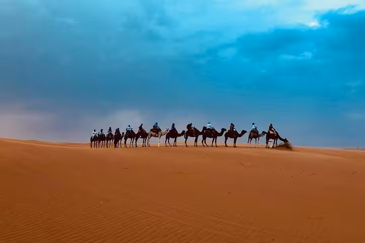 A long camel caravan traverses the dramatic desert under a vibrant sky on the route from Fes to Marrakech.