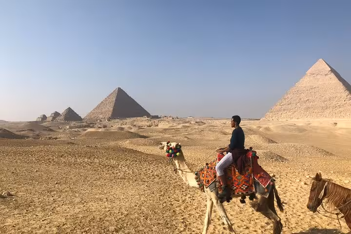 Traveler on camel ride across Giza Plateau with pyramids in view, part of Cairo full-day private trip