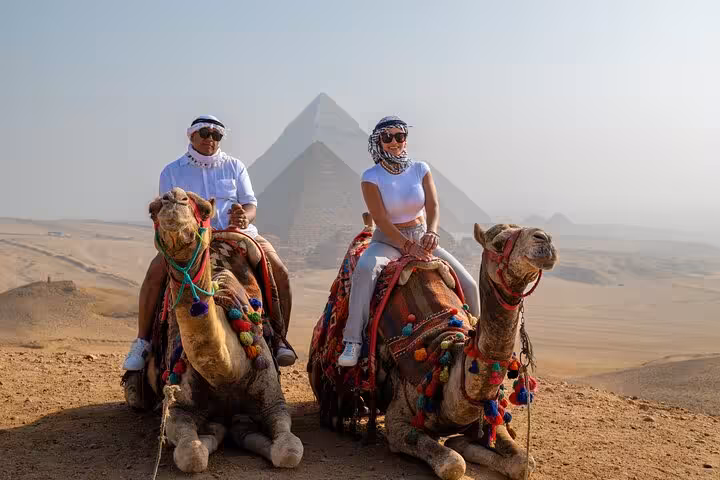 Tourists riding decorated camels by the Giza Pyramids, part of Cairo camel ride and ATV tour combo
