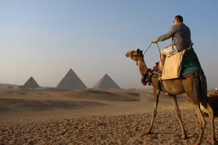 Traveler on a camel ride at sunrise with Giza Pyramids in the background, guided tour with transfers in Cairo