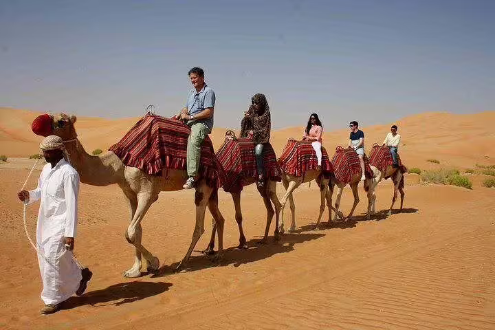 Camel ride in Hurghada desert safari with tourists on camels led by guide across golden sand dunes