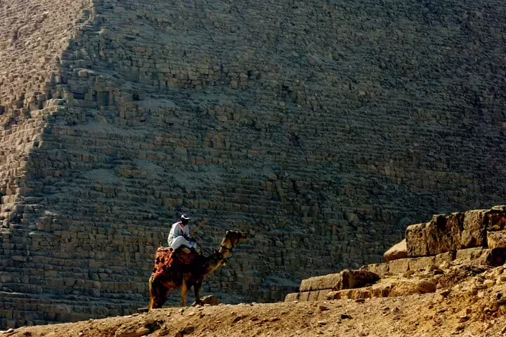 Camel rider passing beside the Great Pyramid of Giza, Egypt, on a desert camel safari day tour