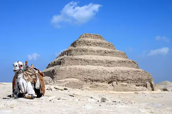 Camel resting near Saqqara Step Pyramid under blue sky on private Dahshur Memphis Saqqara all-inclusive tour