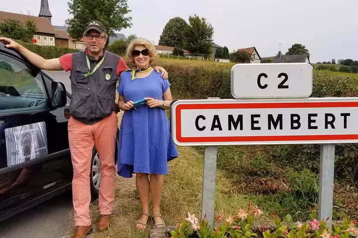 Two tourists posing beside Camembert village road sign in Normandy, France