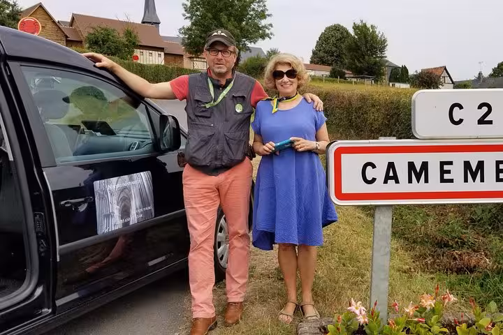 Two tourists posing beside a road sign for Camembert village in Normandy, France