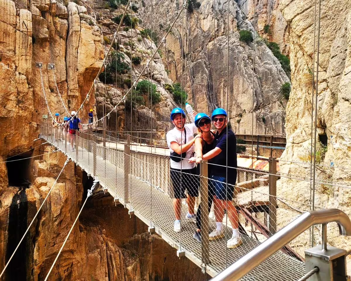Friends in blue helmets on Caminito del Rey suspension bridge, guided group walking tour through El Chorro canyon