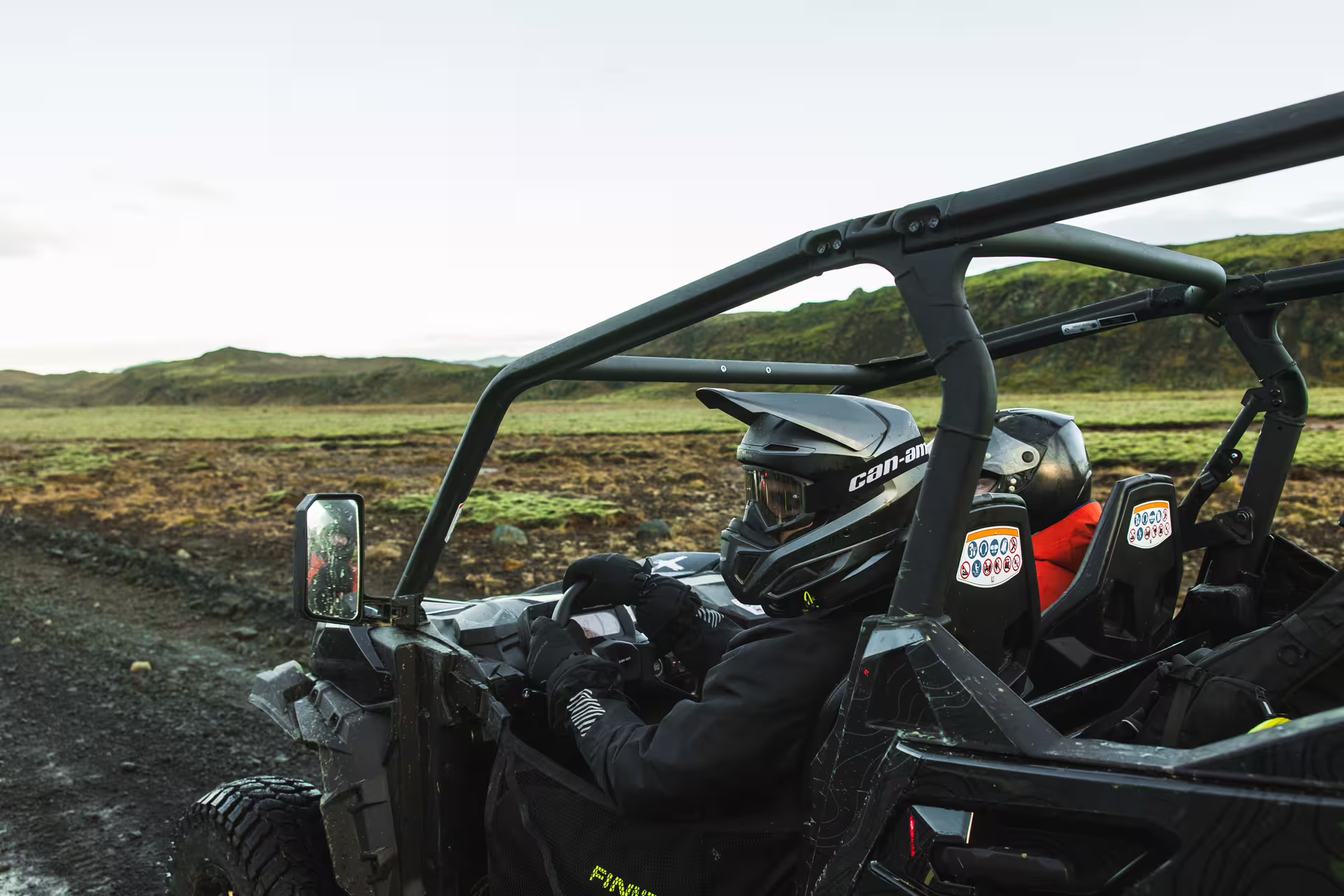 Driver in Can-Am helmet riding a black buggy through volcanic lava fields in Iceland