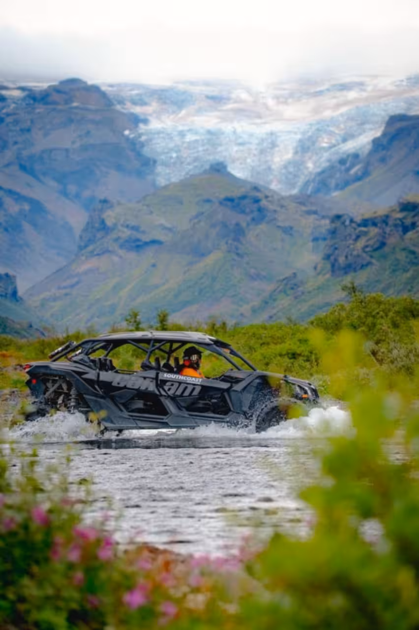 Can-Am buggy crossing a river in Iceland with glacier and green mountains in background