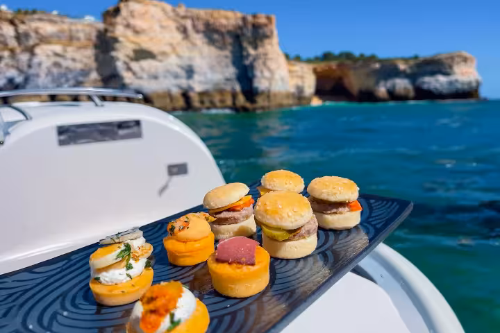 Gourmet food tasting platter with mini burgers and canapes on a boat near Vilamoura caves coastline