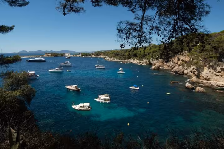 Turquoise bay with white boats anchored near rocky pine-covered cliffs on the French Riviera