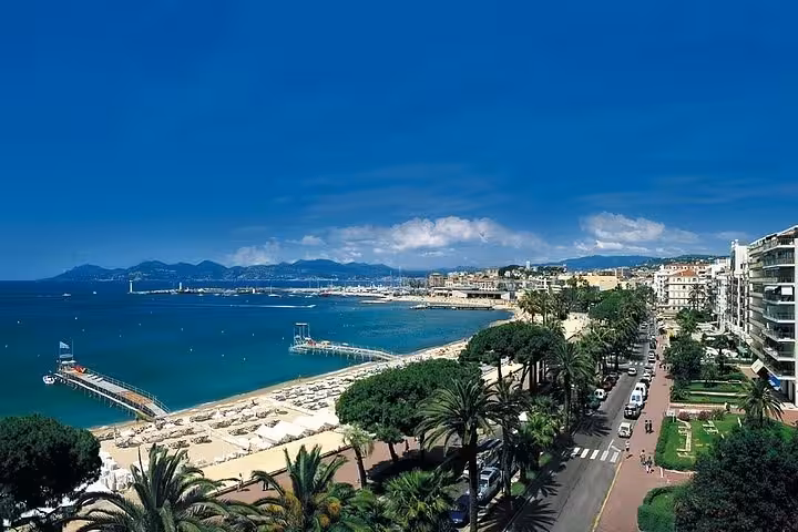 Aerial view of Cannes coastline with sandy beach, palm-lined promenade, and blue Mediterranean Sea