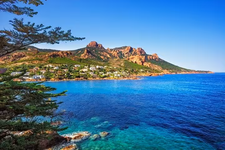 Crystal-clear blue waters along the Côte d'Azur coastline with red rocky hills and seaside villas near Cannes