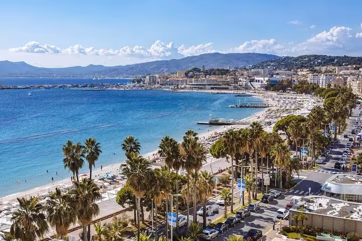 Scenic view of Cannes coastline with palm-lined promenade and azure Mediterranean waters on a sunny day.