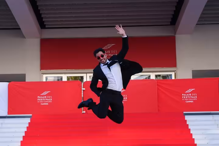 Man in tuxedo jumping joyfully on red carpet steps at Palais des Festivals in Cannes