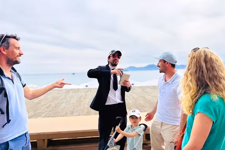 Tour guide in suit directing a small group of tourists near Cannes beachfront promenade
