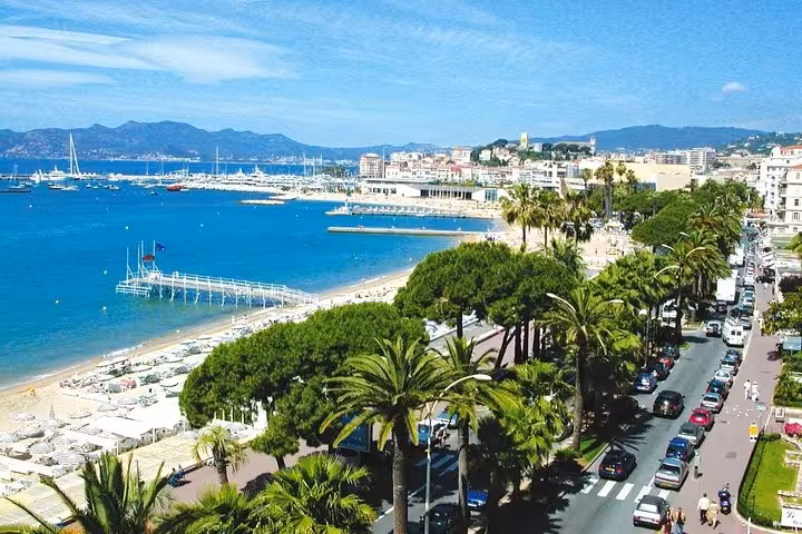 Aerial view of Cannes French Riviera coastline with sandy beach, palm-lined boulevard, and blue Mediterranean Sea