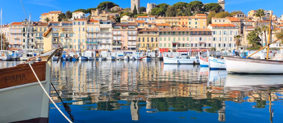Colorful waterfront buildings and boats reflected in the calm harbor of Cannes, French Riviera