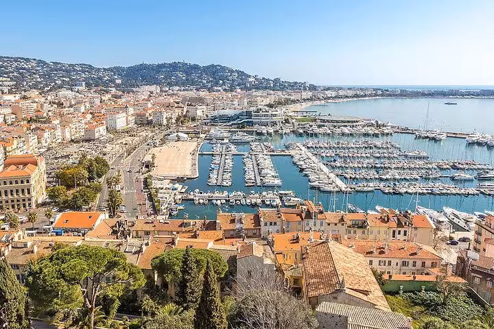 Scenic view of Cannes harbor with luxury yachts and historic architecture under a clear blue sky.