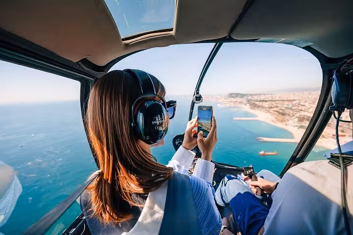 A passenger wearing headphones photographs the stunning Cannes Mediterranean coastline during a private helicopter tour over the French Riviera.