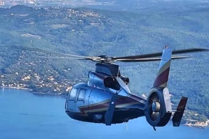 Private helicopter flying over Mediterranean coastline and lush green Alps hills near Cannes
