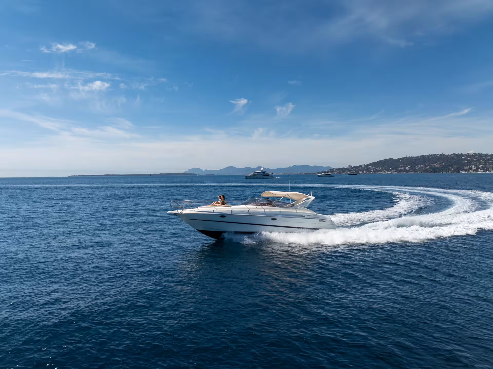 White private yacht speeding through blue Mediterranean waters near Cannes coastline on a sunny day