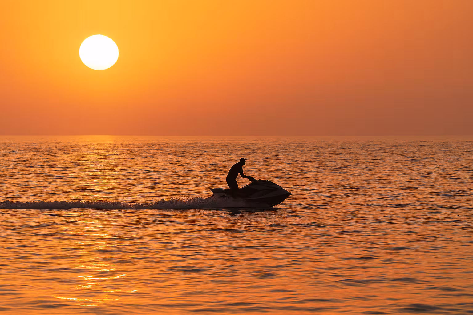 Silhouette of a person riding a jet ski on calm sea at golden sunset near Cannes