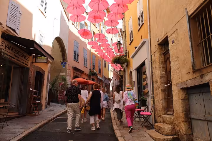 Tourists walking through a charming Provençal village alley decorated with pink umbrellas overhead