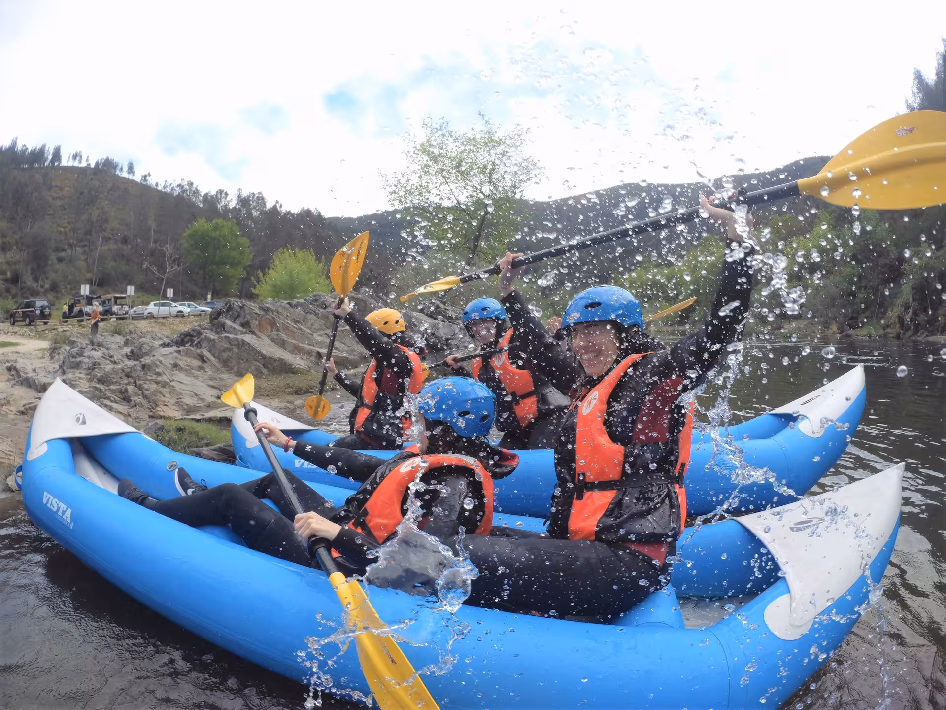 Friends canoe rafting on the Paiva River, Portugal, splashing water and celebrating in inflatable rafts