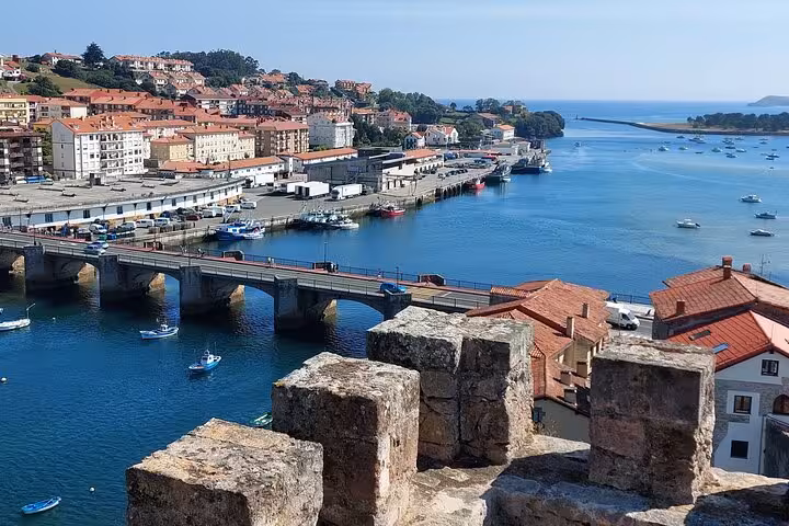 Panoramic view of Cantabria's coastal town with a stone bridge, colorful rooftops, and serene blue waters.