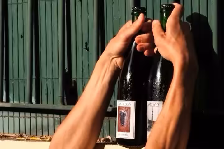 Hands holding two Cantillon wine bottles outdoors during Nice gourmet walking tour