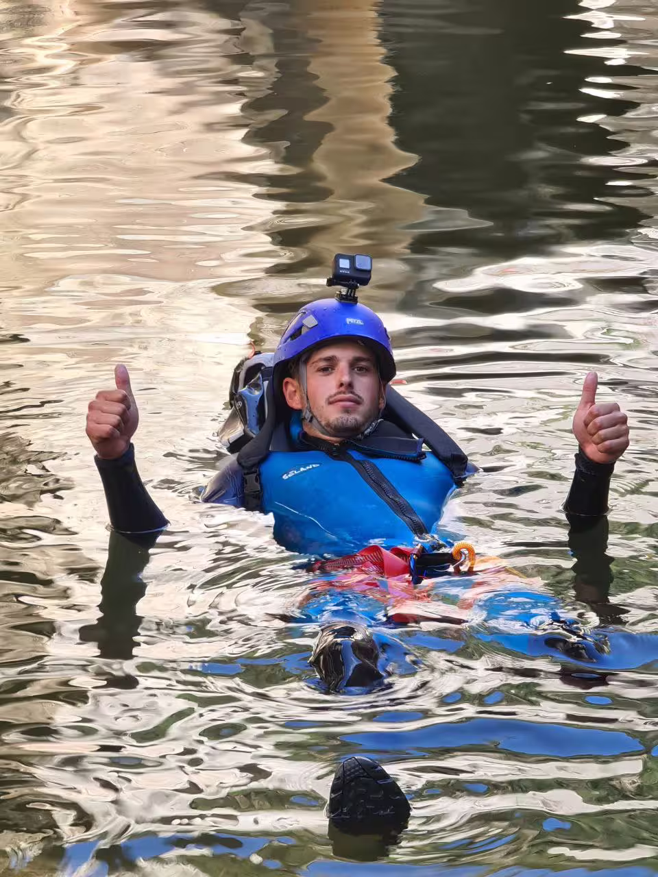 A smiling canyoneer in blue wetsuit and helmet gives thumbs up while swimming in Las Buitreras Canyon Málaga