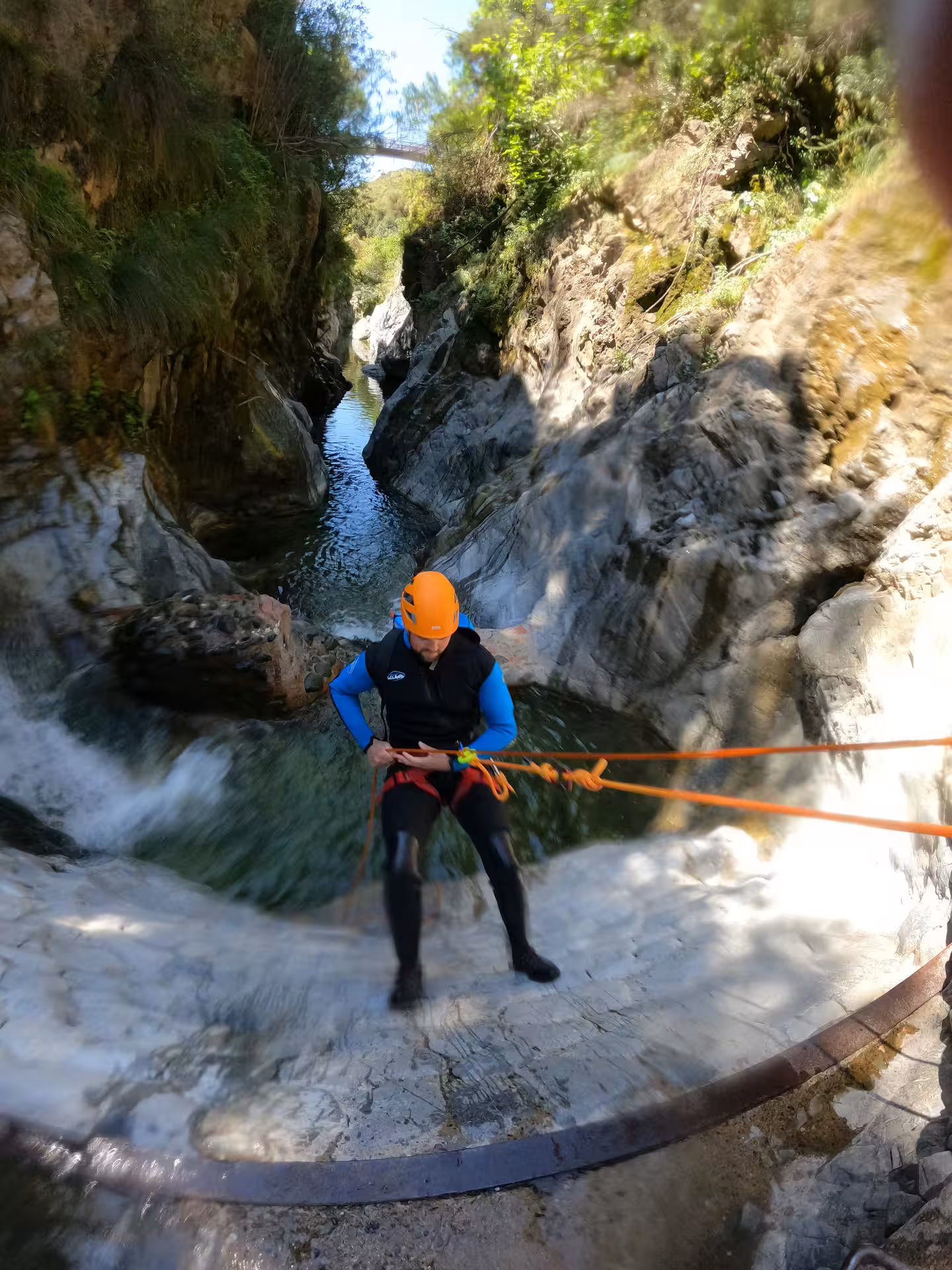 A helmeted canyoner abseils down a smooth rock face above Guadalmina Canyon river in Estepona