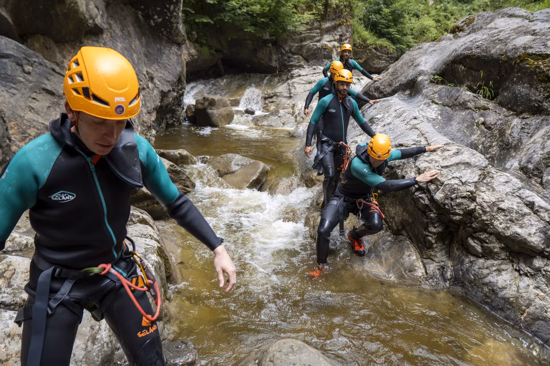 Group of canyoning enthusiasts navigate rocky streams in Chli Schliere, Luzern, equipped with safety helmets.