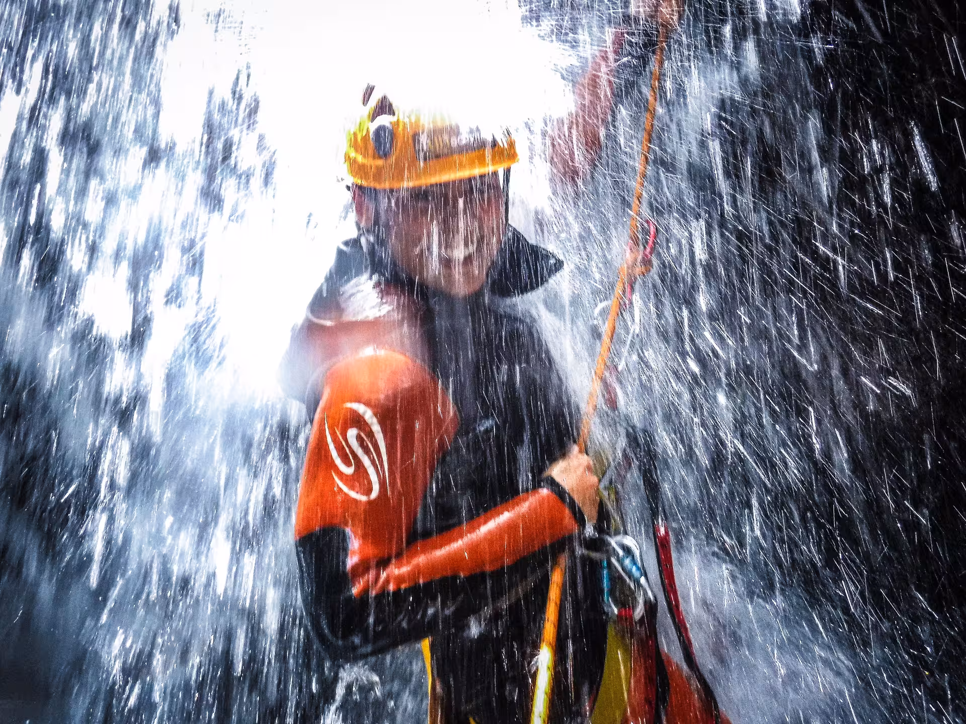 Adventurer canyoning under a powerful waterfall in Furnas, Azores, wearing wetsuit and helmet on a guided rope descent