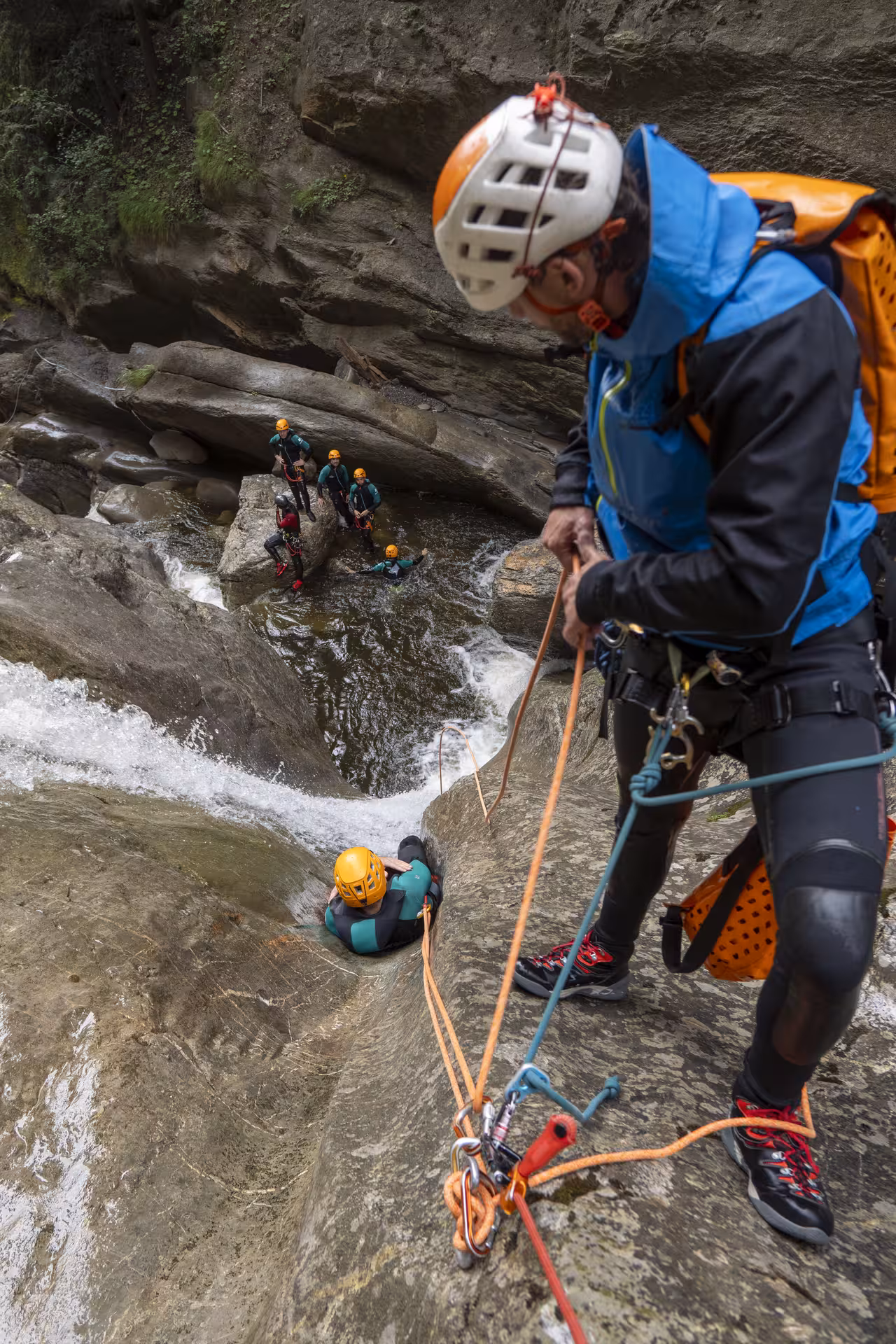 Guide assisting canyoning group with ropes in Chli Schliere's rugged terrain near Luzern, ensuring safety and excitement.