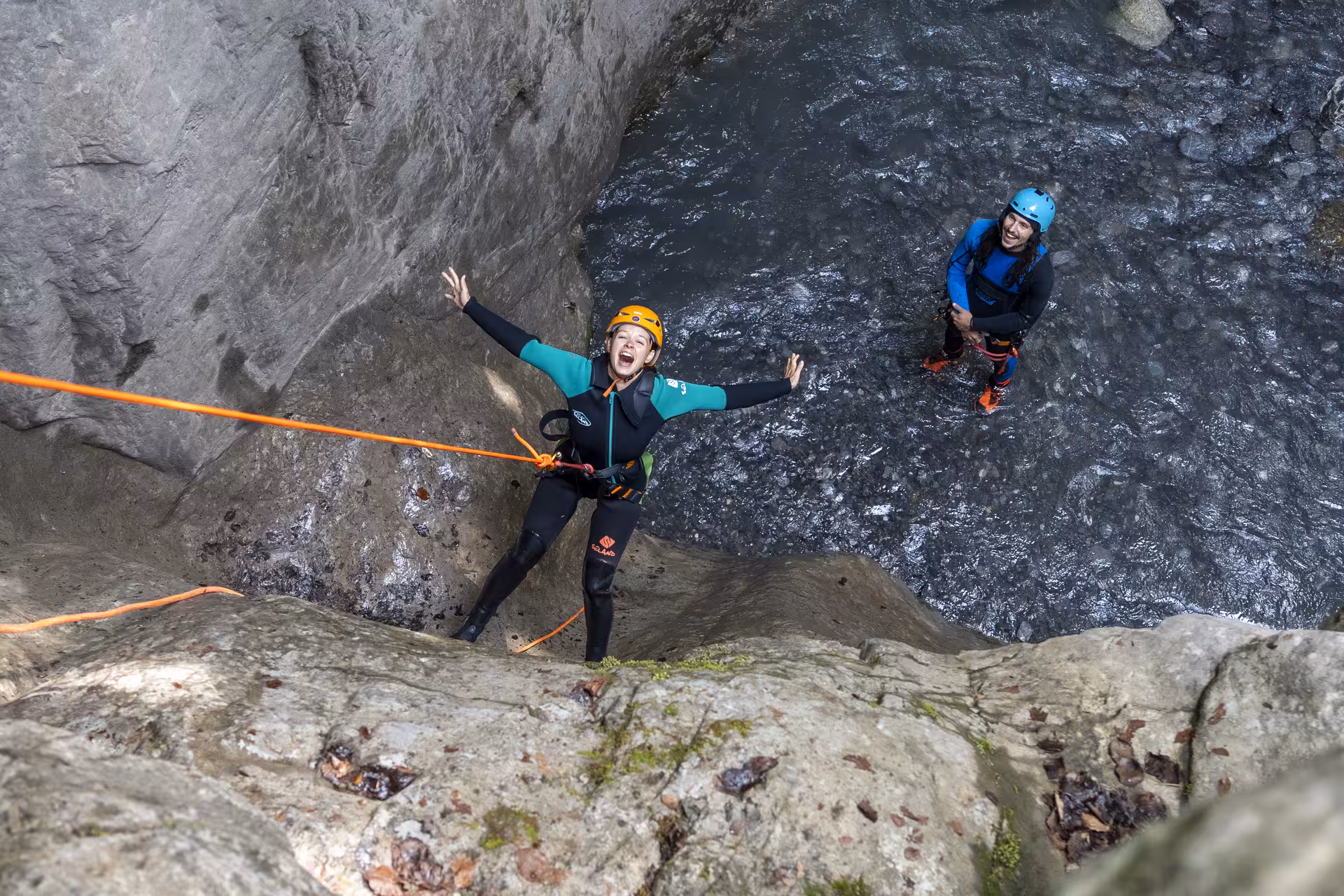 Adventurer joyfully rappelling down a canyon wall during a Canyoning Interlaken tour, surrounded by rocky terrain.